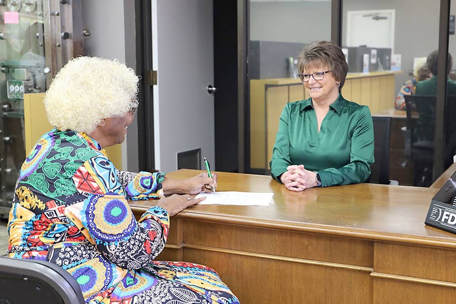 A customer signs a form at a desk in the bank